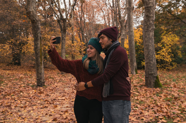 Pareja caucásica tomando una foto en un parque en otoño - Foto, imagen