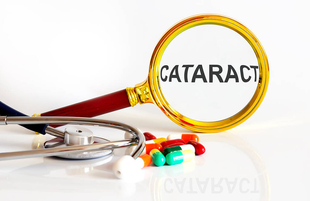 Увеличительная линза с текстом CATARACT с медицинскими инструментами, таблетками - Фото, изображение