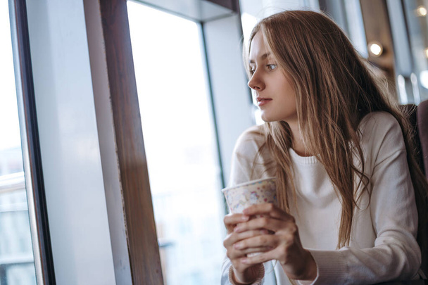 Blonde woman with long blonde hair sitting in cafe and drinking beverage - Photo, Image