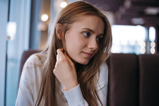  Csinos fiatal nő hosszú szőke hajjal ül a kanapén egy kávézóban. - Fotó, kép