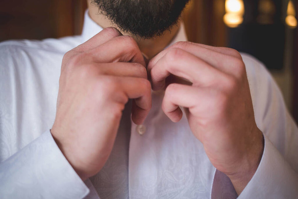 A closeup of an adult male buttoning up a white shirt with a blurry background - Foto, Imagem
