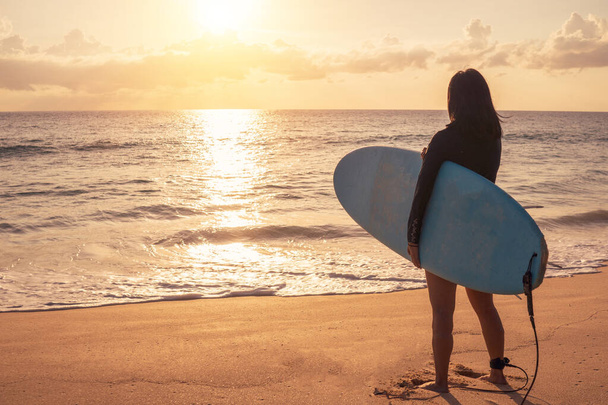 Silueta surfařské ženy nesoucí jejich surfovací prkna na pláži západ slunce se slunečním světlem pozadí - Fotografie, Obrázek