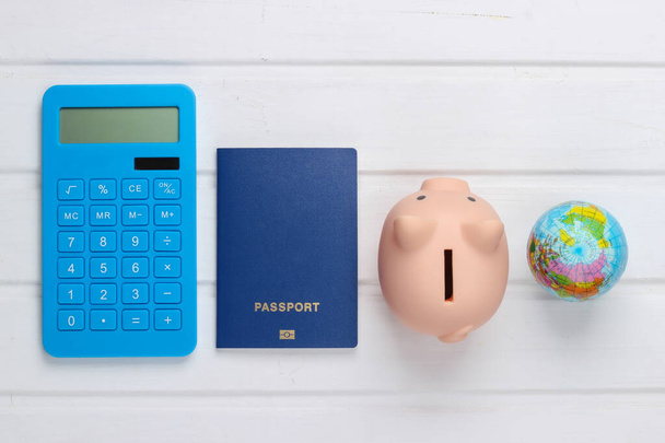 Viagem ou emigração. Passaporte com banco porquinho, globo e calculadora sobre fundo branco de madeira. Vista superior. Depósito plano - Foto, Imagem