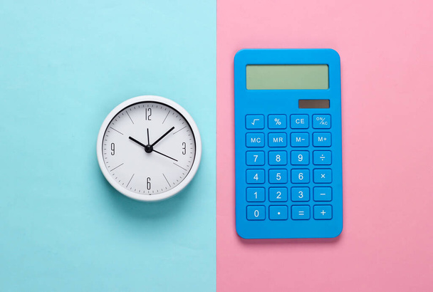 Biały zegar i kalkulator na niebieskim różowym tle. Minimalistyczne ujęcie studyjne. Widok z góry - Zdjęcie, obraz