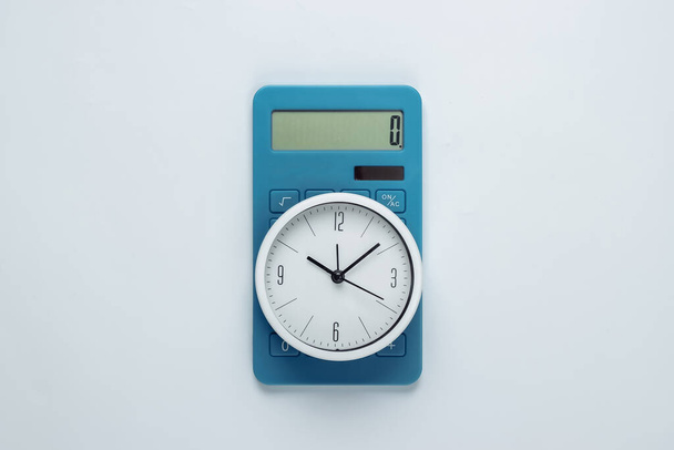 Bílé hodiny a kalkulačka na bílém pozadí. Minimalistický studiový záběr. Horní pohled - Fotografie, Obrázek