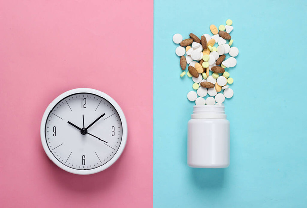 Time to take pills. White clock with bottle of pills on blue-pink pastel background. Top view. Flat lay - Photo, Image