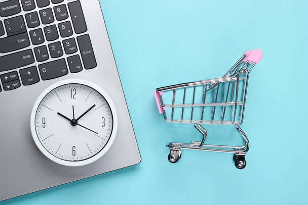 Tiempo de compras en línea. Teclado de ordenador con reloj y carrito de supermercado sobre fondo azul. Vista superior - Foto, imagen