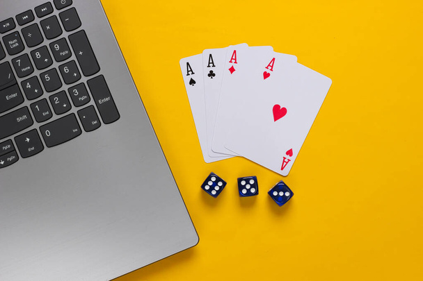 黄色の背景に4つのエース、サイコロとラップトップキーボード。オンラインポーカーカジノ。ゲーム中毒だ。トップ表示 - 写真・画像