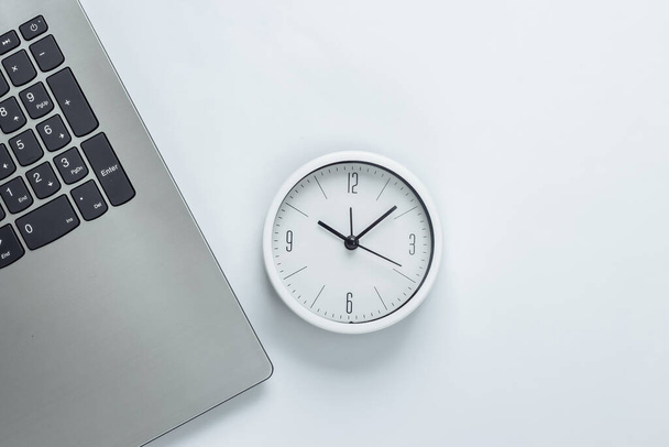 Laptop y reloj sobre fondo blanco. Tiempo huyendo. El concepto de plazos urgentes en el trabajo y compromisos. Vista superior - Foto, imagen