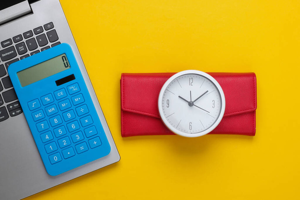 Tijd om geld te verdienen. Online zaken. Witte klok, laptop, rekenmachine en rode portemonnee op gele achtergrond. Bovenaanzicht. Vlakke plaat - Foto, afbeelding