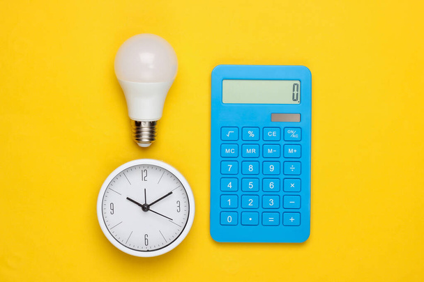 Relógio com lâmpada, calculadora sobre um fundo amarelo. Minimalismo. Vista superior - Foto, Imagem