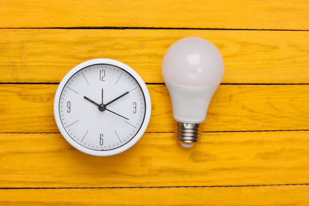 Clock with light bulb on yellow wooden background. I have an idea! Minimalism. Top view - Photo, Image