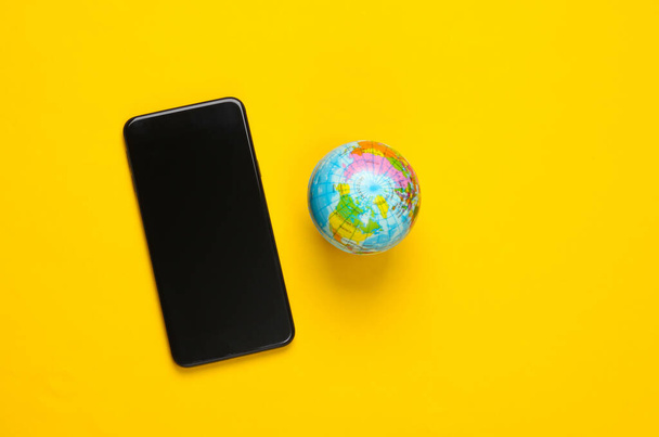 黄色の背景にスマートフォンや地球。グローバルネットワーク。世界中のモバイル通信。5Gグローバルネットワーク - 写真・画像