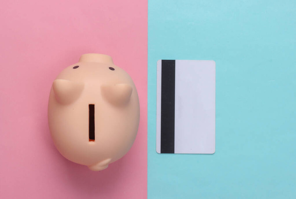 Piggy banco com cartão de crédito em um fundo pastel azul-rosa. Vista superior. Depósito plano - Foto, Imagem