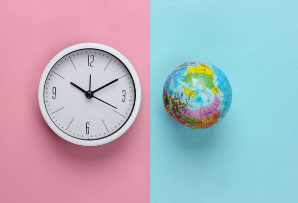 Ρολόι και σφαίρα σε ροζ μπλε παστέλ φόντο. Παγκόσμια ώρα. Άνω όψη - Φωτογραφία, εικόνα