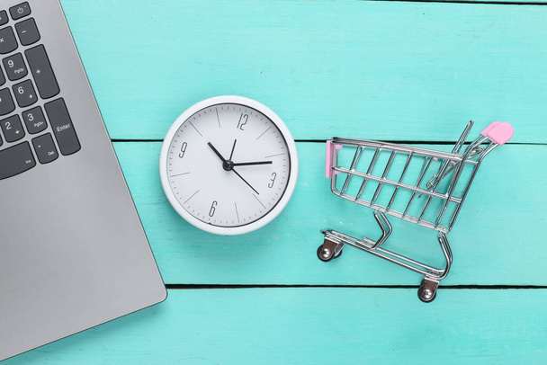 Tempo di shopping online. Tastiera per computer con orologio e carrello supermercato su sfondo blu in legno. Vista dall'alto - Foto, immagini