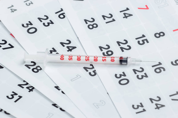 Siringa su un calendario mensile primo piano. Vaccinazione - Foto, immagini