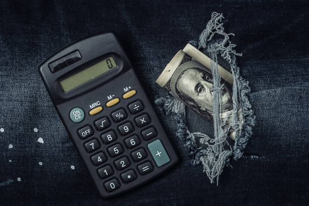 Kalkulator i sto dolarowy banknot w podarty dżinsy dziura - Zdjęcie, obraz