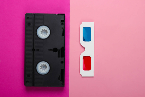 Anaglif jednorazowego papieru 3d okulary i kasety wideo na różowym tle. Retro media, rozrywka lat 80-tych. Widok z góry - Zdjęcie, obraz