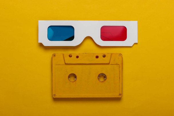 Anaglif jednorazowego papieru 3d okulary i kasety audio na żółtym tle. Retro media, rozrywka lat 80-tych. Widok z góry - Zdjęcie, obraz