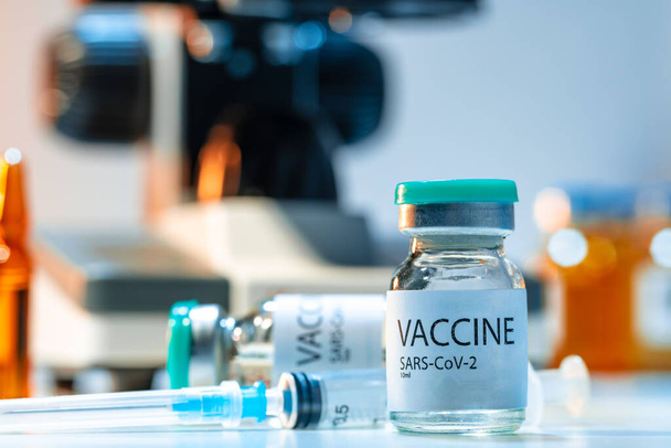 Vial of Covid-19 vaccine next to a microscope - Фото, изображение