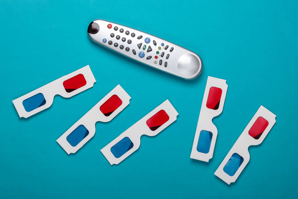 Many Anaglyph disposable paper 3d glasses and tv remote on  blue background. Tv time. Top view - Foto, Bild