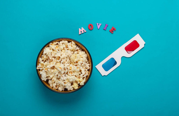 Movie time. Stereoscopic anaglyph disposable paper 3d glasses and popcorn on blue background. Top view - Photo, Image