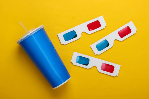 Movie time. Stereoscopic anaglyph disposable paper 3d glasses, paper cup of drink on yellow background. Top view - Photo, Image