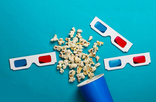 Movie time. Cardboard bucket of popcorn and Stereoscopic anaglyph disposable paper 3d glasses on blue background. Top view - Photo, Image