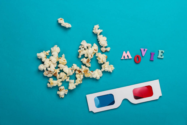 Filmzeit. Stereoskopische Anaglypheneinwegpapier-3D-Brille mit Popcorn auf blauem Hintergrund. Ansicht von oben - Foto, Bild
