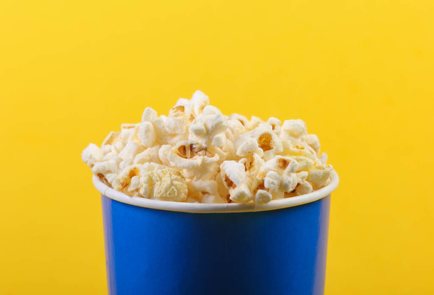 Movie time. Cardboard bucket of popcorn on yellow background. - Photo, Image