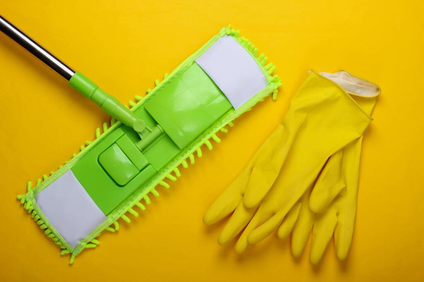 Plastikowy zielony mop, rękawiczki na żółtym tle. Dezynfekcja i czyszczenie w domu. Widok z góry - Zdjęcie, obraz