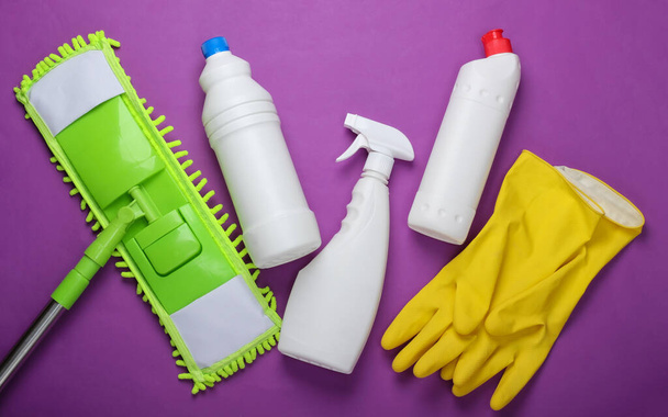 Środki czyszczące. Plastikowy zielony mop, rękawiczki, butelki detergentu na fioletowym tle. Dezynfekcja i czyszczenie w domu. Widok z góry - Zdjęcie, obraz