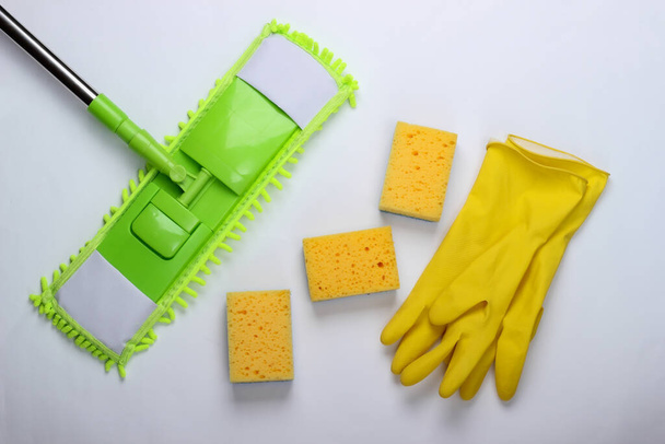 Reinigungsmittel. Grüner Wischmopp aus Plastik, Handschuhe und Schwämme auf weißem Hintergrund. Desinfektion und Reinigung im Haus. Ansicht von oben - Foto, Bild