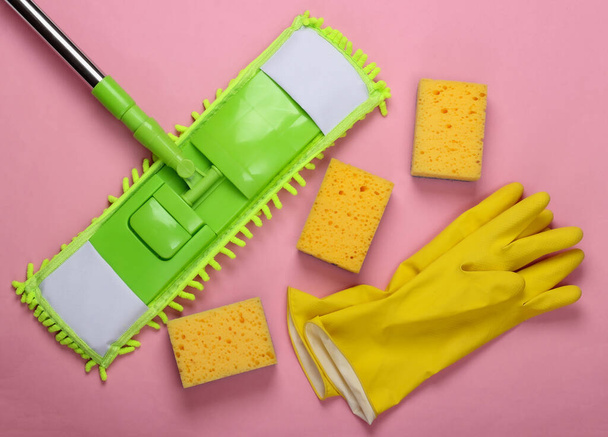 Schoonmaakmiddelen. Plastic groene dweil, handschoenen en sponzen op roze ondergrond. Desinfectie en schoonmaken in het huis. Bovenaanzicht - Foto, afbeelding