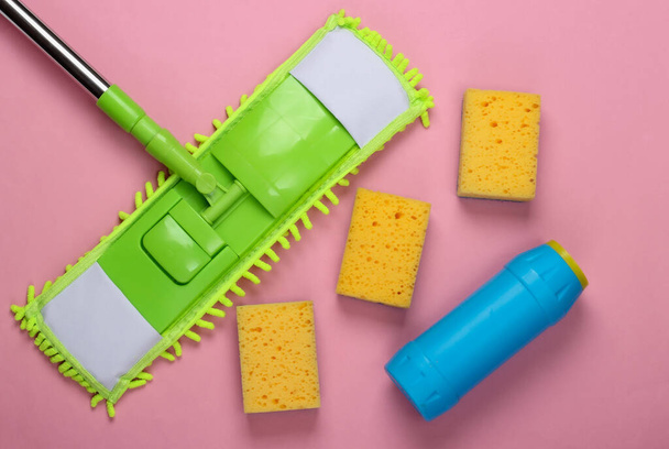 Reinigungsmittel. Grüner Wischmopp aus Plastik, Schwämme, eine Flasche Waschmittel auf rosa Hintergrund. Desinfektion und Reinigung im Haus. Ansicht von oben - Foto, Bild