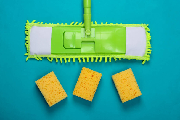Cleaning products. Plastic green mop and sponges on blue background. Disinfection and cleaning in the house. Top view - Photo, Image