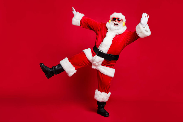 Full length photo of pensioner old man grey beard hands up open mouth entartainer wear santa costume x-mas coat belt sunglass headwear earphones black boots isolated red color background - Valokuva, kuva