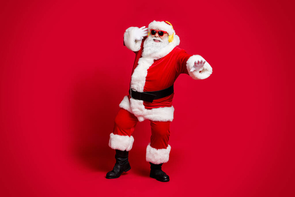 Full length photo of retired old man grey beard retro dancing carefree old people discotheque attract snow maidens wear santa costume sunglass headwear boots isolated red color background - 写真・画像