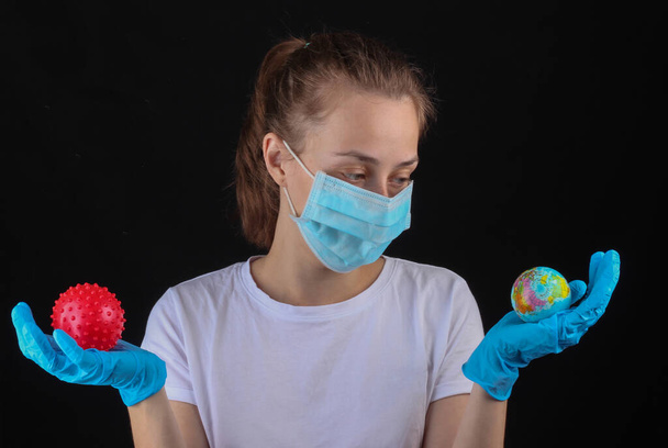 Vrouw met een medisch beschermend masker, handschoenen houden wereldbol en virus stam model op een zwarte achtergrond. - Foto, afbeelding