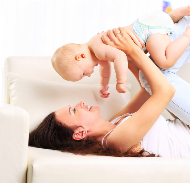 Happy beautiful young mother and baby laying on sofa - Foto, afbeelding