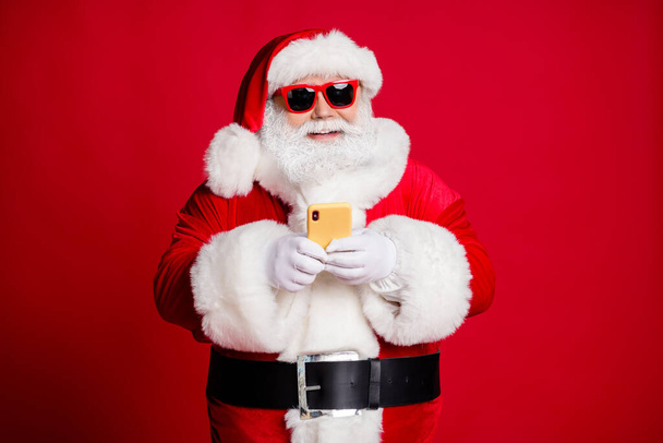 Portrait of his he nice handsome focused cheerful bearded Santa using device 5g blogging typing congratulation congrats web app store shop isolated bright vivid shine vibrant red color background - Fotó, kép