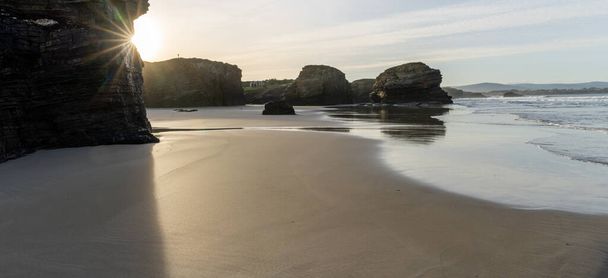 Ένα πανόραμα της αμμώδους παραλίας και των οδοντωτών βράχων στη Γαλικία το ηλιοβασίλεμα - Φωτογραφία, εικόνα
