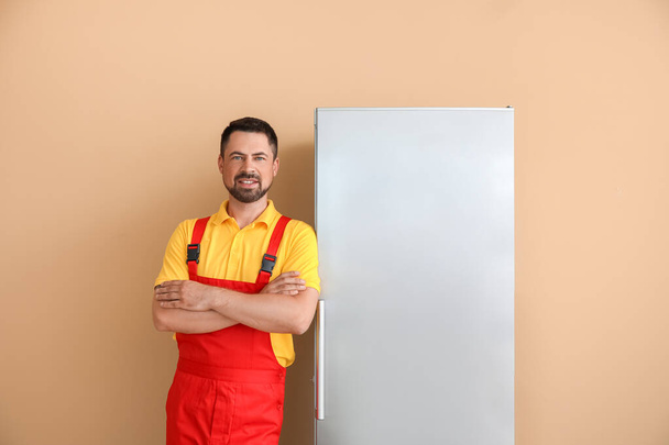 Arbeiter des Reparaturdienstes in der Nähe des Kühlschranks auf farbigem Hintergrund - Foto, Bild