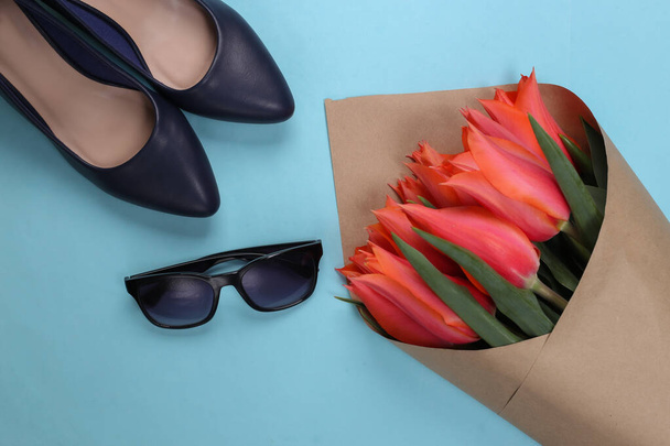 Bouquet of tulips, high-heeled shoes with sunglasses on blue background. Top view. Flat lay - Photo, Image