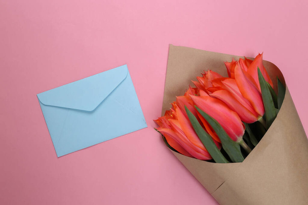 Bouquet of red tulips with an envelope on pink pastel background. Valentine's Day. Top view - Photo, Image