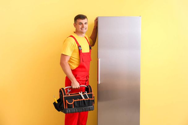 Worker of repair service near fridge on color background - Foto, afbeelding