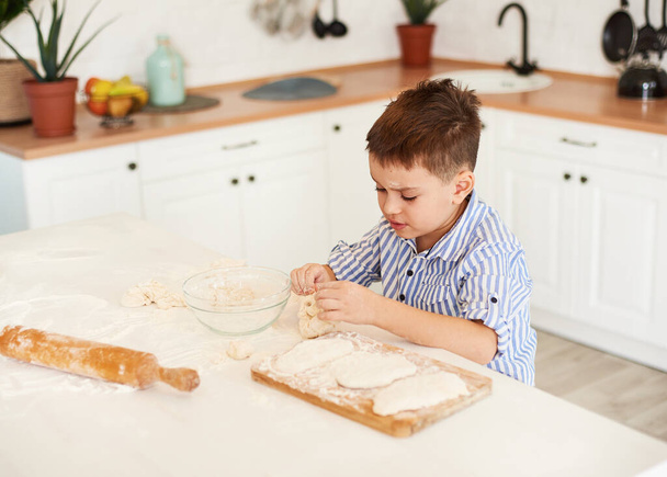 A fiú leül a konyhaasztalhoz, és készít valamit a tésztából.. - Fotó, kép