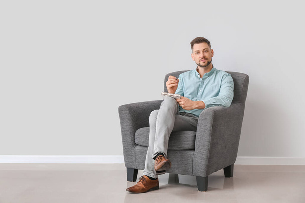 Άνδρας ψυχολόγος κάθεται στην πολυθρόνα κοντά στο φως τοίχο - Φωτογραφία, εικόνα