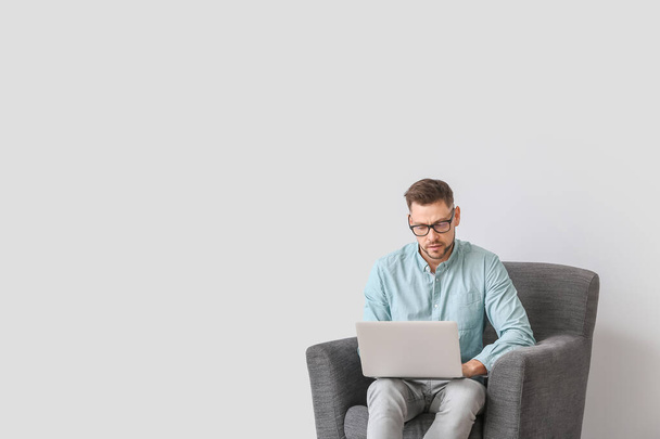 Psicologo maschile con computer portatile seduto in poltrona su sfondo chiaro - Foto, immagini